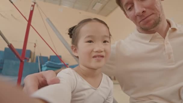 ハンドヘルドPov胸は 体操と振付訓練後にクラスで休むコーカサス男性コーチと自分自身のビデオを記録するアジアの少女のショット — ストック動画