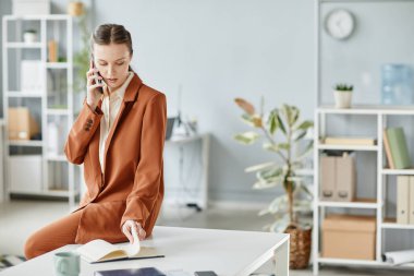 Beyaz ofis içinde masa başında otururken akıllı telefondan konuşan genç bayan patronun minimal portresi, boşluğu kopyala