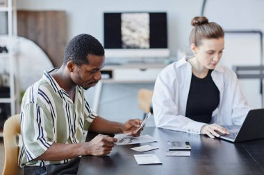 Fotoğraf stüdyosundaki resimlere bakan genç siyahi fotoğrafçıların yan görünüm portresi.