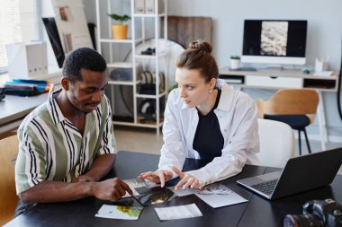 Stüdyoda birlikte çalışırken basılı resimleri tartışan iki genç fotoğrafçının portresi