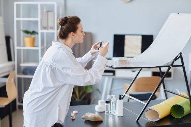 Fotoğraf stüdyosunda akıllı telefonla fotoğraf çeken genç bir kadın fotoğrafçının yan görüş portresi