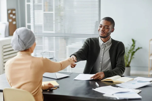 Portrait of young black man shaking hands with female HR manager after successful job interview in office, copy space