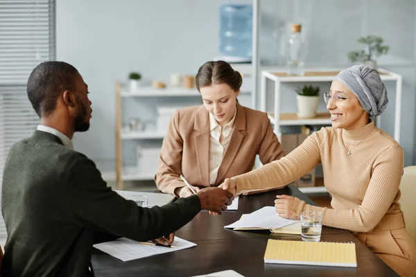 Diverse group of people in meeting or job interview at office setting, focus on Middle Eastern woman shaking hands with candidate