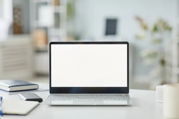 Background image of opened laptop with white screen mockup at workplace in minimal office interior white and grey tones, copy space