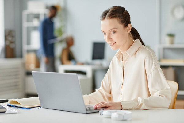 Portrait of smiling young woman using laptop at office workplace in minimal interior, copy space