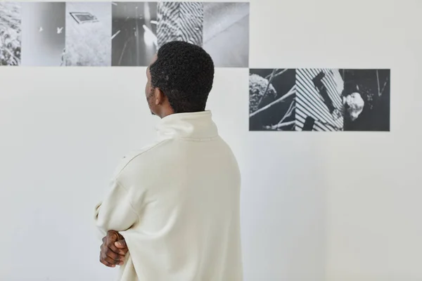 Minimal back view of unrecognizable black man looking at art in photo gallery, copy space