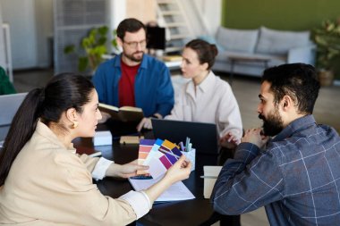 Genç bayan tasarımcı renk paletine işaret ederken aynı zamanda iki iş arkadaşına karşı çalışma toplantısında iş arkadaşınla projeyi tartışıyor.