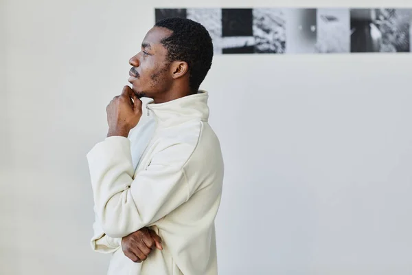 Minimal side view portrait of handsome black man looking at images in photo gallery and enjoying art