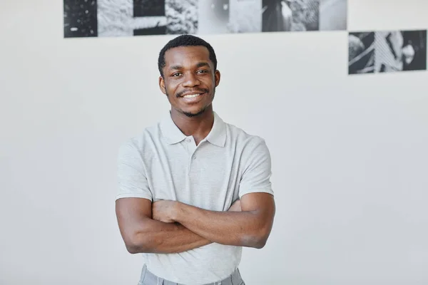 Minimal waist up portrait of young black artist smiling at camera while standing with arms crossed in gallery hall, copy space