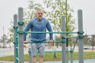 Paralel parmaklıklarda egzersiz yapan kararlı olgun bir adamın ön görünüm portresi, boşluğu kopyala