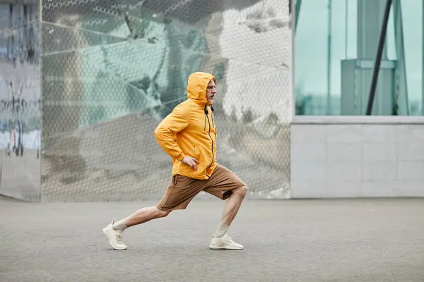 Minimal side view portrait of sportive mature man stretching outdoors in urban city setting and wearing contrasted yellow jacket