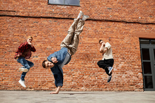 Freeze frame of all male breakdancing team jumping in air and posing against brick wall