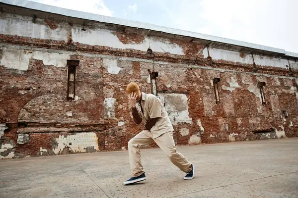 Minimal wide angle shot of young man dancing hip-hop outdoors in shabby urban setting and hiding face