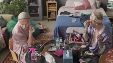 İpek bornozlu iki çekici beyaz adamın makyaj yapıp sohbet ederken dağınık bir apartman dairesinde gösteri yapmaya hazırlandığı orta boy bir fotoğraf.