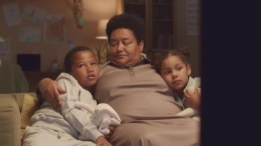 İki torunu olan, rahat pijama giyen ve elinde pelüş oyuncaklar olan olgun Afro-Amerikan bir kadının akşamları televizyon karşısında oturup film izlediği orta boy bir fotoğraf.
