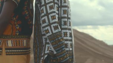 Kumlu çölde mavi gökyüzünün altında sırtüstü durup etrafa bakan Afro-Amerikan parlak elbiseli genç çiftin portresini kaldırın.