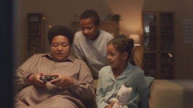 İki neşeli Afrikalı Amerikalı kardeşle büyükannelerinin video oyunu oynayıp, akşamları rahat bir ev ortamında kanepede oturarak eğlendikleri orta boy bir yavaşlama.