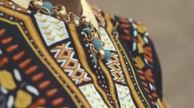 Geleneksel kıyafetler ve aksesuarlar giymiş özgüvenli, Afro-Amerikan kadınının yavaş yavaş çekilmiş portresini öne doğru çevirin. Arkaplanı bulanık kum tepecikleriyle dolu.