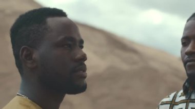 İki Afro-Amerikalı erkek ve bir kadının, kumlu çölde açık mavi gökyüzünün altında daireler çizerek dikilirken ağır ağır portrelerini çek.