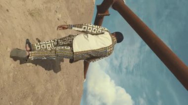 Güneşli bir günde çölde tek başına kumlu tepelere tırmanan parlak bir tulum giymiş Afro-Amerikan yerlisinin dikey görünümü.