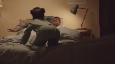 İki Afro-Amerikan ergen kardeşin güzel pijama giyip ninelerinin geceleri yatakta masal okumasını dinledikleri orta boy bir fotoğraf.