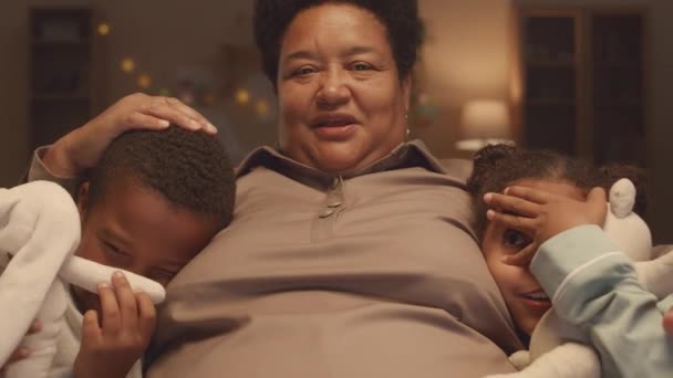 2人の恐ろしいアフリカ系アメリカ人の兄弟のスローモーを待って 彼らの間に座って慰めている祖母と一緒にテレビでホラー映画を見ながら手で目を閉じます — ストック動画