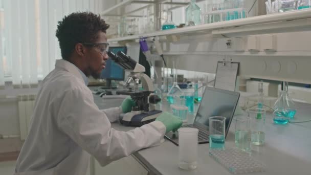 Afrika Kökenli Amerikalı Erkek Biyokimyacının Mikroskop Kullanırken Laboratuarda Çalışırken Kimyasal — Stok video