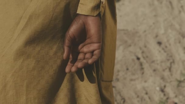一个穿着长长的亚麻黄长袍 手反手站在沙地里的难以辨认的非裔美国人 他的动作慢吞吞地站在地上 — 图库视频影像