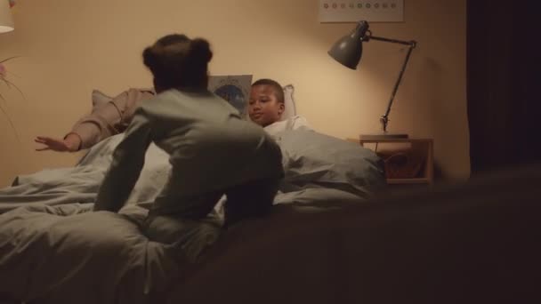 2人のアフリカ系アメリカ人の兄弟が夜にベッドでおばあちゃんの読書に耳を傾け かわいいパジャマを着ている中型ショット — ストック動画
