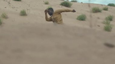 Kum tepeciğinde koşan ve gülen uzun sarı cüppeli aktif Afrikalı Amerikalı adamın görüntüsü.