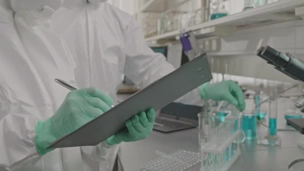 Nakloněný Snímek Páru Mikrobiologů Ochranných Uniformách Respiračních Maskách Provádějících Výzkum — Stock video