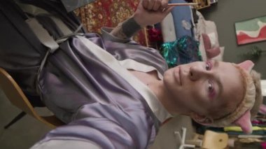 Dikey çekimde, evde makyaj yaparken kameraya konuşan Kafkas asıllı tuhaf bir adam görülüyor.