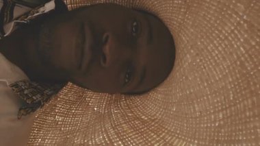 Dikey göğüs hizasında büyük hasır şapkalı ve süslü gömlekli yakışıklı Afro-Amerikan bir adamın portresi. Güneş ışığı altında duran kameraya bakıyor ve açık mavi gökyüzü.