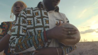 Çölde yalnız başına dikilen güzel karısı arkasında dururken Afrikalı Amerikalı adamın djembe davuluna hafifçe vurması.