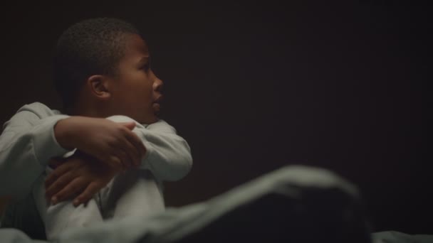一个惊慌失措的非洲裔美国小男孩坐在床上 蜷缩在黑暗的房间里 灯光摇曳着 — 图库视频影像