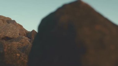 Uzun kollu sarı bornoz giyen özgür Afrikalı Amerikalı adam gün batımında kollarını kayanın tepesine açmış duruyor.