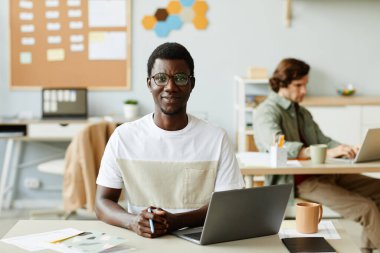 Ofiste çalışan ve kameraya gülümseyerek bakan hevesli bir gencin portresi.