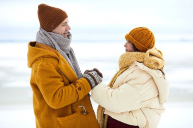 Kış manzarasında el ele tutuşan romantik genç çiftin yan görünüm portresi, flört veya evlenme teklifi konsepti