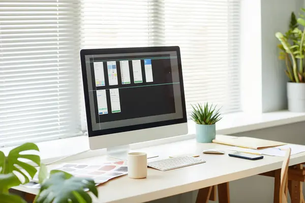 Minimal background image of computer with mobile app designs on screen at workplace table