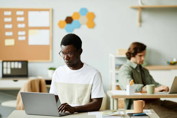 Minimal portrait of young black man using laptop in office or coworking space, copy space