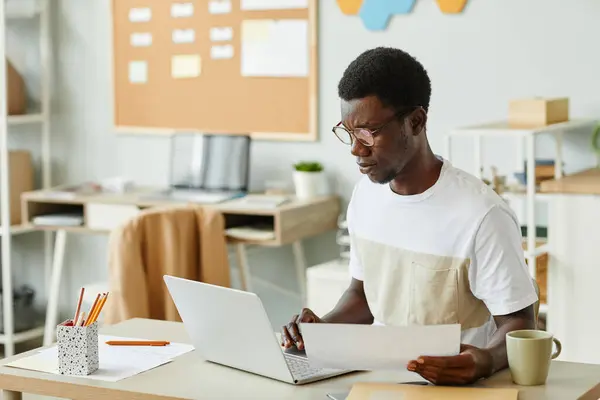 Minimal portrait of black young man wearing glasses while working with laptop at office workplace, copy space