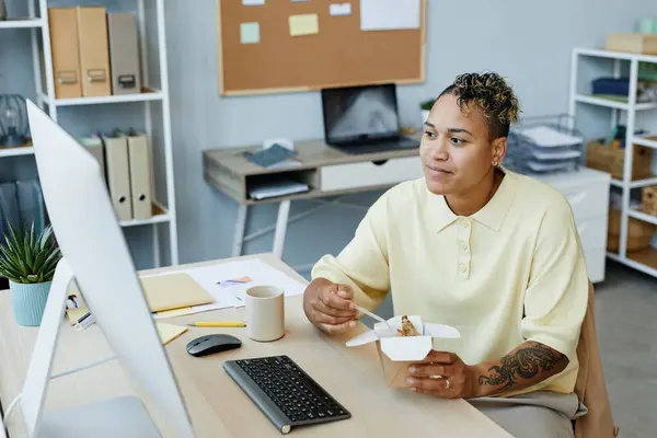 Portrait of tattooed black woman eating takeout noodles at workplace during lunch break, copy space