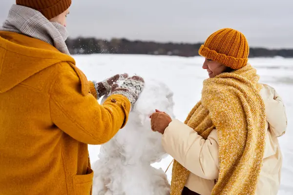 Close up of young couple building snowman together while enjoying winter fun outdoors