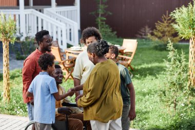 Büyük Afrikalı Amerikalı bir ailenin portresi. Tekerlekli sandalyede oturmuş yaz partisinde dışarıda sohbet ediyorlar.