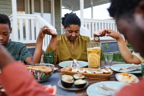 アフリカ系アメリカ人の若い女性の肖像画は 家族が集まって手を握っている間に屋外のテーブルで優雅さを言います — ストック写真