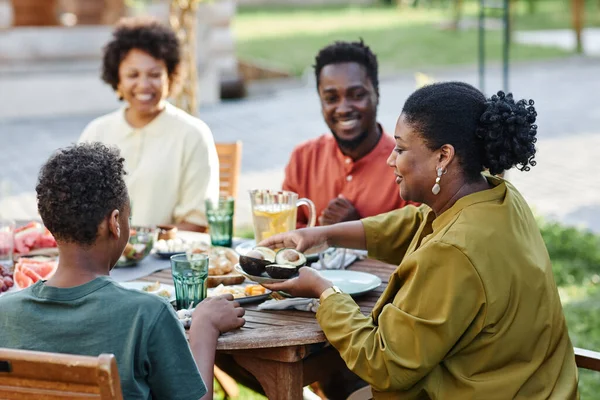 年轻黑人女子在户外与家人共进晚餐时 为家人提供健康食物的侧景肖像 — 图库照片