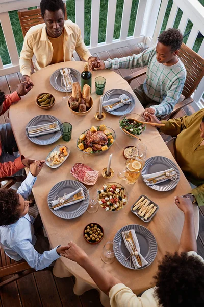 Top view of African American family saying grace at festive dinner table outdoors and holding hands in cozy setting
