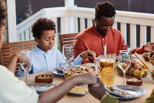 Portrait of black father and son praying at dinner table with family and holding hands