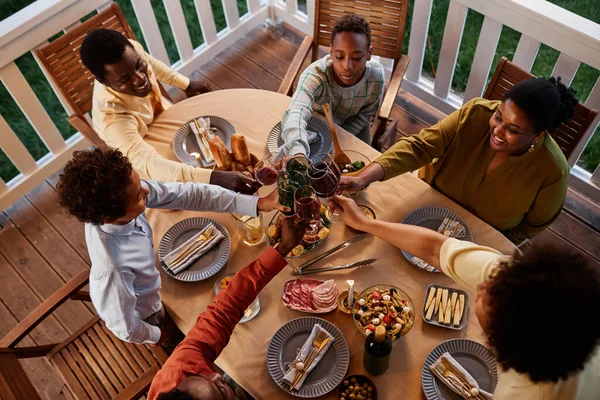 在舒适的夜景中 非洲裔美国人大家庭在户外餐桌边的酒杯上挂着高角镜 — 图库照片