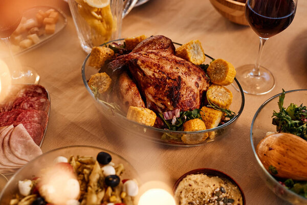 Close up of roasted chicken on dinner table with rustic homemade dishes in cozy setting